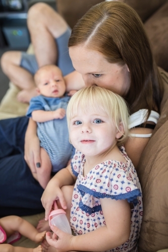 Mother kissing daughter on top of head while holding newborn baby boy - Australian Stock Image