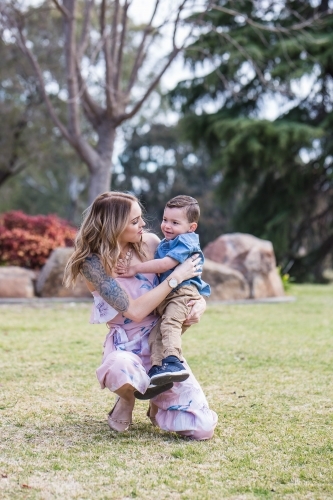 Mother kneeling down smiling at mixed race aboriginal caucasian boy in arms - Australian Stock Image