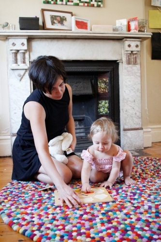 Mother kneeling on floor with her baby girl doing a puzzle - Australian Stock Image