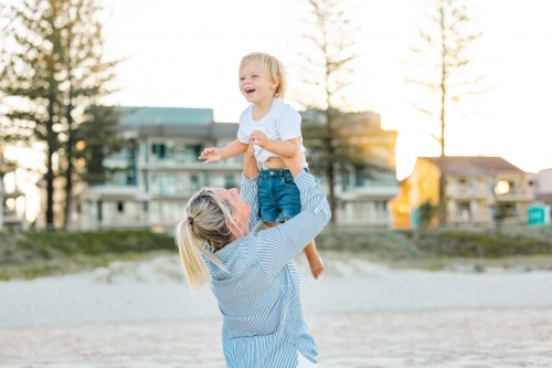 Mother lifting toddler son, playing on Gold Coast beach - Australian Stock Image
