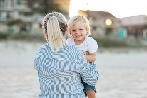Mother lifting toddler son, playing on Gold Coast beach - Australian Stock Image