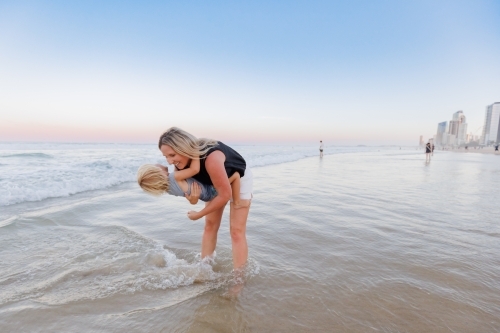 Mother lowering son into water on the beach at the Gold Coast - Australian Stock Image