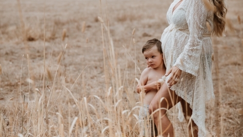 Mother pregnant with second child standing with son in brown grass outside