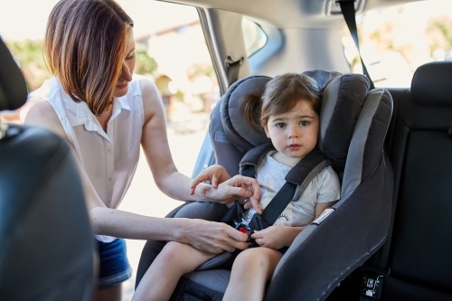 Mother putting daughter in forward facing car seat - Australian Stock Image