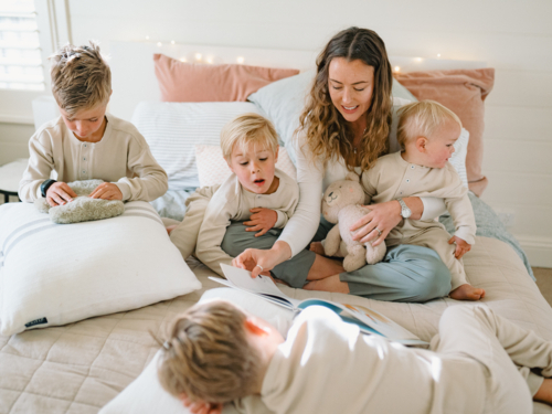Mother reading a bedtime story with kids around the bed - Australian Stock Image