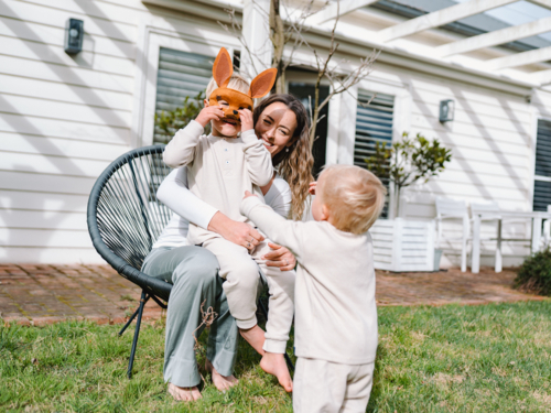 Mother sitting with kids in backyard boy and toddler child playing and wearing kangaroo mask - Australian Stock Image