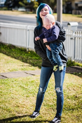 Mother standing in yard laughing holding child - Australian Stock Image