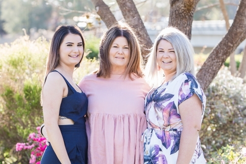 Mother standing smiling with arms around two daughters - Australian Stock Image