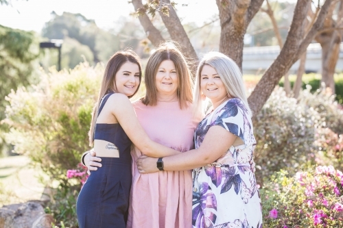 Mother standing with arms around two daughters hugging and smiling - Australian Stock Image