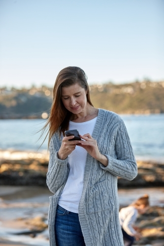Mother using phone at seaside - Australian Stock Image