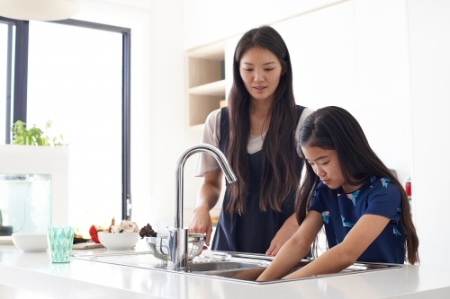 Mother watching over daughter whilst washing hands in sink - Australian Stock Image