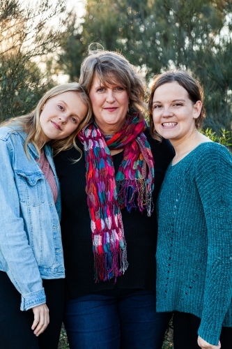 Mother with her two daughters hug together outside - Australian Stock Image