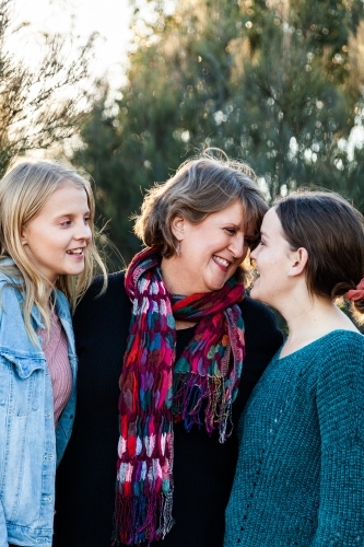 Mother with her two daughters hug together outside - Australian Stock Image