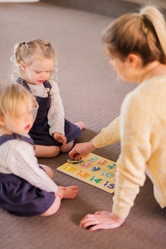 Mother with two young girls playing puzzles on lounge room floor - Australian Stock Image
