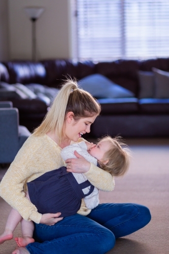 Mother wrestling with little girl tickling and laughing together in lounge room - Australian Stock Image