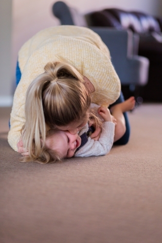 Mother wrestling with little girl tickling and laughing together in lounge room - Australian Stock Image