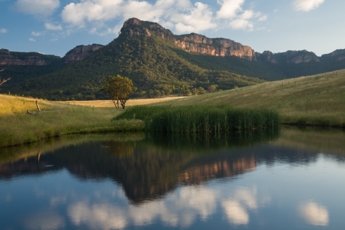 Mountain, paddock and sky reflected in farm dam water