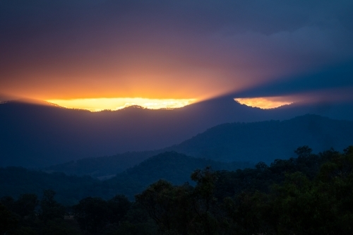 Mountains with sun rays piercing clouds at sunset - Australian Stock Image