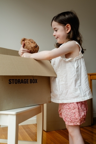 Moving house - Young girl holding her beloved teddy bear inside a cardboard storage box