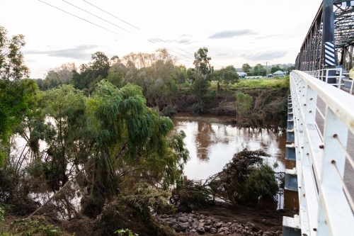 muddy flattened trees along riverbank after flash flooding - Australian Stock Image