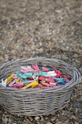 Multi coloured clothes pegs in a wicker basket with a pebble background