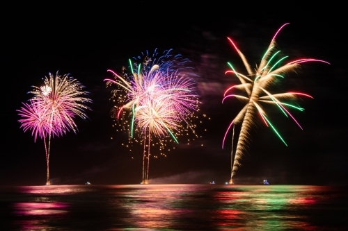 Multi coloured fireworks exploding over an ocean in the night sky. - Australian Stock Image