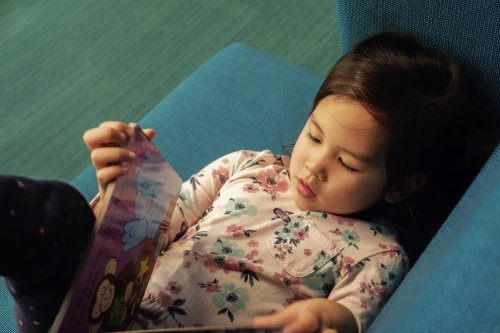 Multicultural child girl reading a book in library