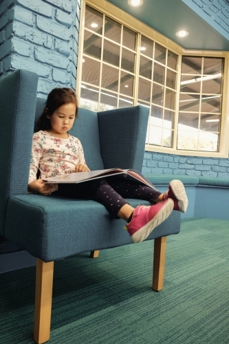 Multicultural child reading a book in library - Australian Stock Image