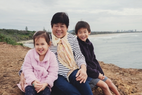 Multicultural grandchildren hug Asian grandmother - Australian Stock Image