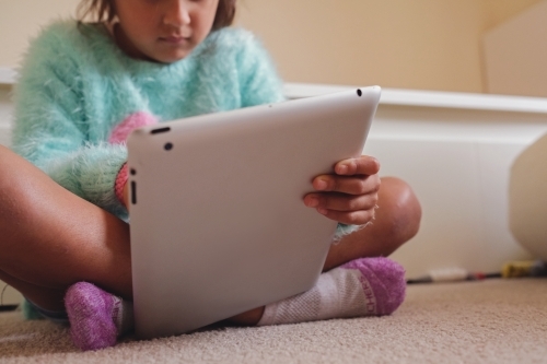 Multicultural kid using tablet in bedroom - Australian Stock Image