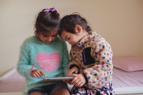Multicultural kids using tablet in bedroom - Australian Stock Image