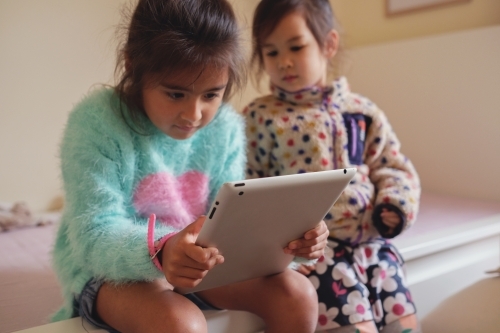 Multicultural kids using tablet in bedroom - Australian Stock Image
