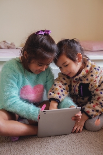 Multicultural kids using tablet in bedroom - Australian Stock Image