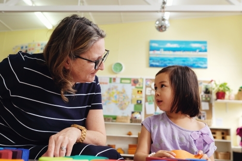 Multicultural teacher and child playing wooden blocks puzzles in kindergarten - Australian Stock Image