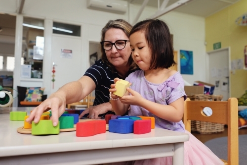 Multicultural teacher and child playing wooden blocks puzzles in kindergarten
