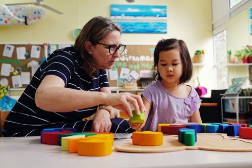 Multicultural teacher and child playing wooden blocks puzzles in kindergarten - Australian Stock Image