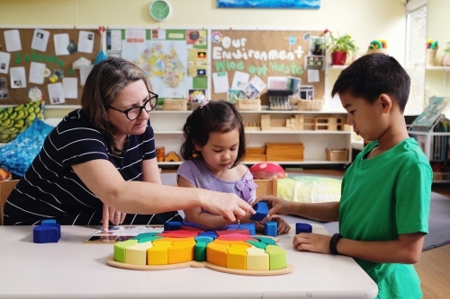 Multicultural teacher and children playing wooden blocks puzzles in kindergarten - Australian Stock Image
