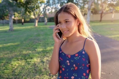 Multiethnic teenage girl using phone in the park - Australian Stock Image