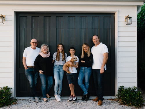 Multigenerational family standing outside in front of black garage door - Australian Stock Image
