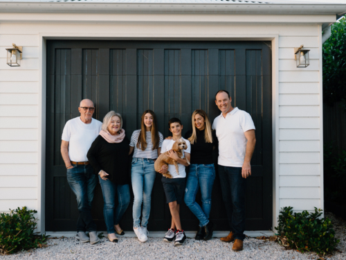 Multigenerational family standing outside in front of black garage door - Australian Stock Image