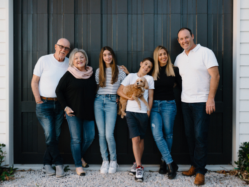 Multigenerational family standing outside in front of black garage door - Australian Stock Image