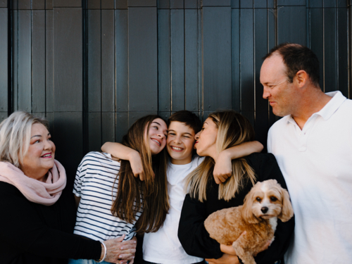 Multigenerational family standing outside in front of black garage door - Australian Stock Image
