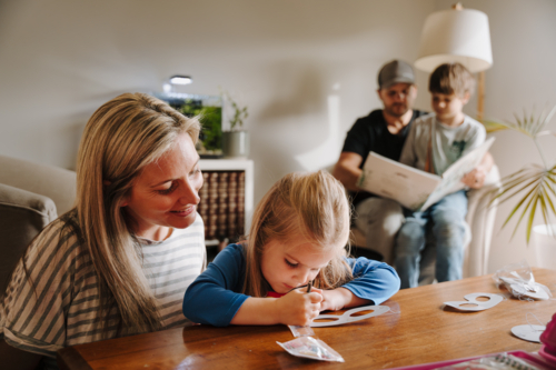 Mum helping daughter with her artwork on the table. - Australian Stock Image