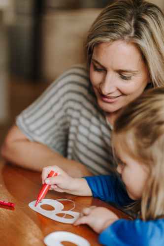 Mum helping daughter with her artwork on the table. - Australian Stock Image