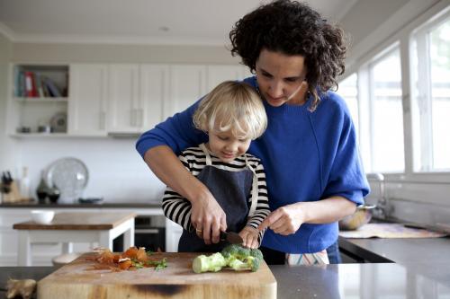 Mum helping young boy cut vegetables - Australian Stock Image