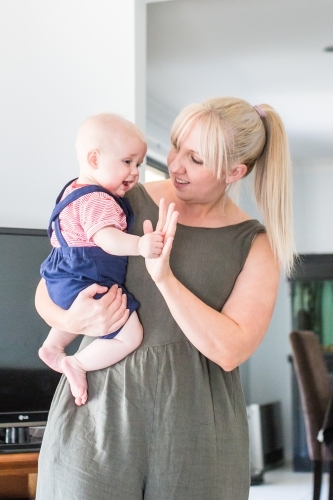 Mum holding baby boy in arms giving high five smiling - Australian Stock Image