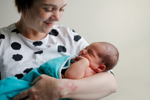 Mum holding her sleeping newborn, smiling - Australian Stock Image