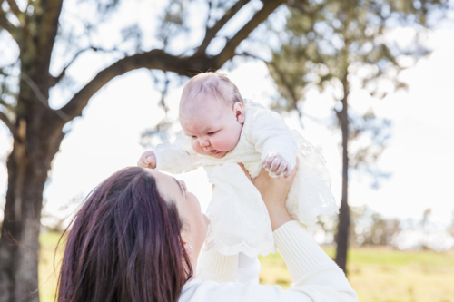 Mum holding newborn baby in the air laughing - Australian Stock Image