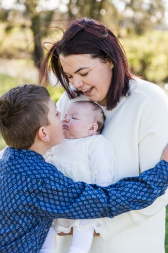 Mum holding newborn daughter while older brother kisses sister - Australian Stock Image