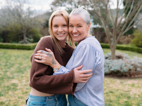 Mum hugging teenage daughter while standing in the backyard of their new home - Australian Stock Image